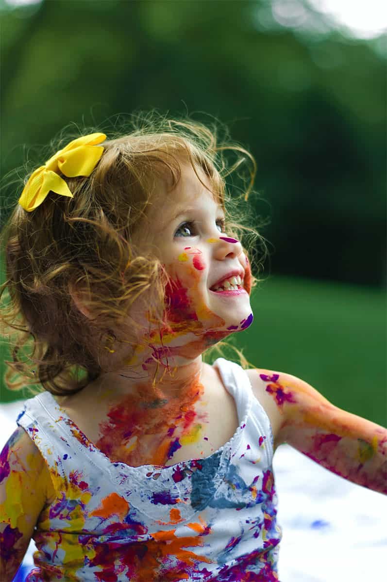 Niña pintada de colores, con sus pinceles en la mano